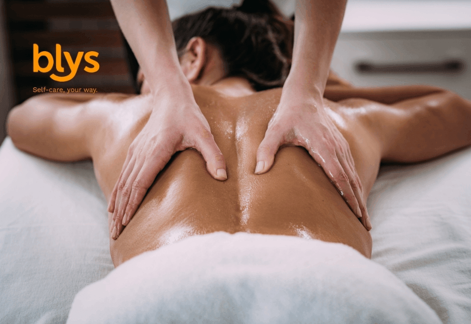 A client lies face down for a relaxing lomi lomi massage, with an oil-slicked back, therapist’s hands, and white towel in a spa setting.