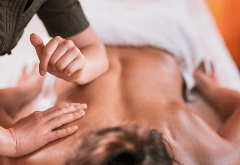 A massage therapist gives a sports massage to a person lying face down as hands massage their bare back, creating a calm, deep wellness scene.