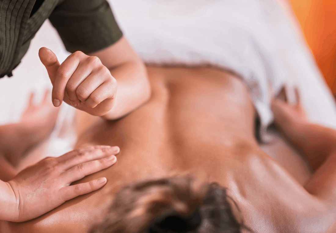 A massage therapist gives a sports massage to a person lying face down as hands massage their bare back, creating a calm, deep wellness scene.