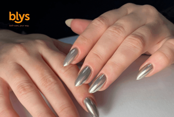Close-up of hands with long, almond-shaped metallic silver chrome nails resting on a pale surface, showcasing a sleek, polished manicure.