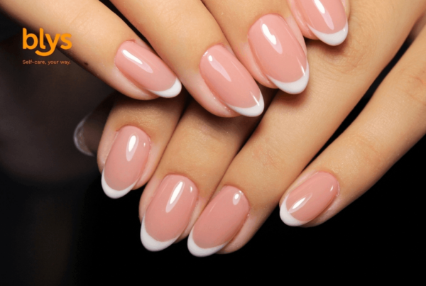 Close-up of manicured hands with glossy pink-and-white acrylic nails layered against a black background, conveying elegance and polish.