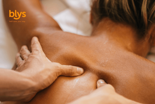 Close-up of a person receiving a soothing back massage, with hands pressing shoulder muscles in warm, tranquil lighting; blys logo visible.