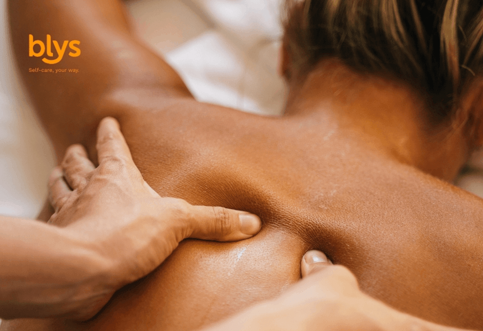 Close-up of a person receiving a soothing back massage, with hands pressing shoulder muscles in warm, tranquil lighting; blys logo visible.