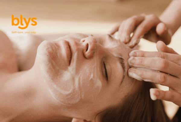 Relaxed woman receives a soothing facial massage with creamy cleanser as a skincare professional gently works across her forehead; blys logo visible.