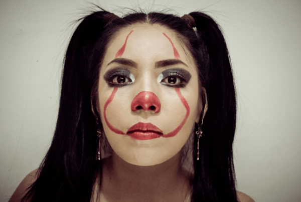Close-up portrait of a woman with black pigtails and clown makeup; her neutral gaze feels somber and unsettling.