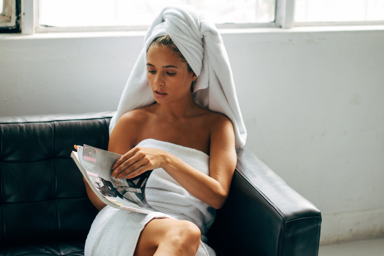 Woman sitting on couch in towel and reading a magazine