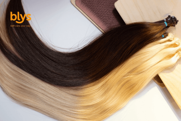 Close-up of a hairstylist adding hair extensions to blonde hair with a comb and clips, showcasing precise salon technique in a polished, professional setting.