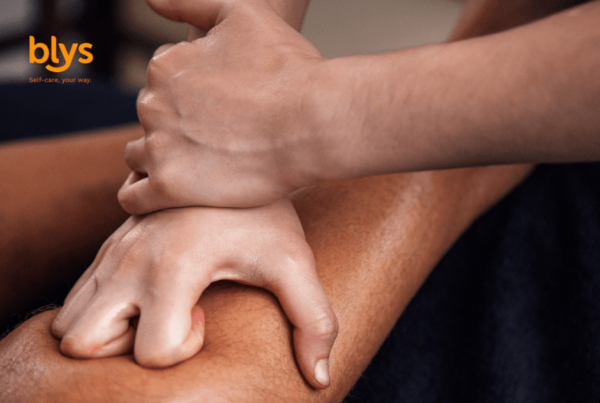 Close-up of hands applying firm massage pressure to a person, conveying relaxation, wellness, and therapeutic self-care; Blys logo visible.