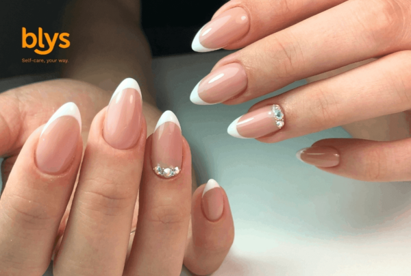 Close-up of hands showing elegant pink almond-shaped French-manicured nails with sparkling rhinestone accents, creating a polished, glamorous beauty look.