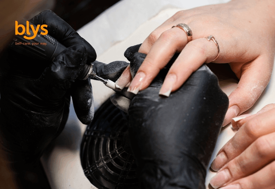 Close-up of a nail technician in black gloves performing Russian manicure with an electric file on a client’s long manicured nails, conveying precision and care.