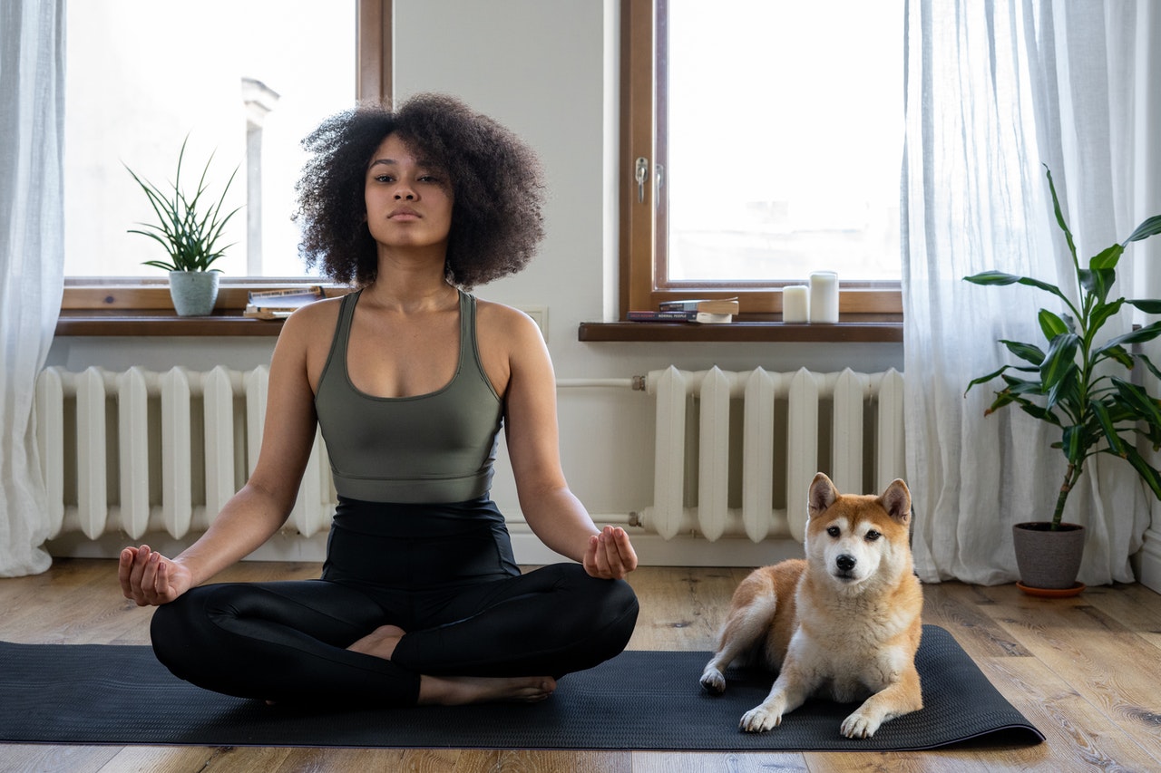 7 ways to have the best staycation ever - learn to meditate - woman and her dog sitting on yoga mat in home. Woman is meditating