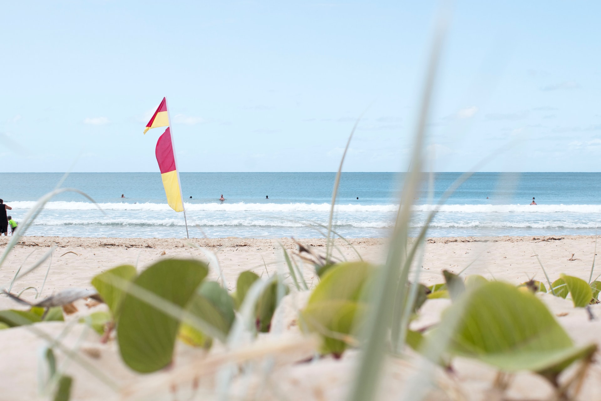 7 ways to have the best staycation ever - catch some rays - Australian beach with lifeguard flags and people jumping in waves in the distance