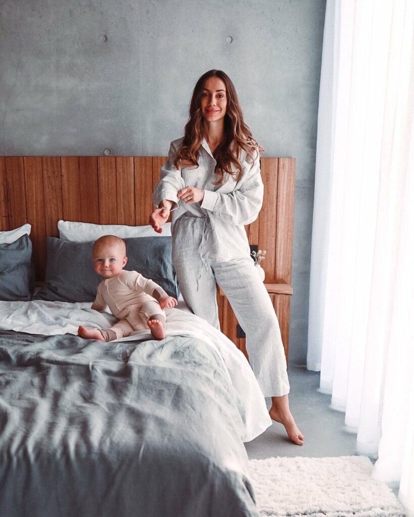 Woman standing next to bed and baby is on bed