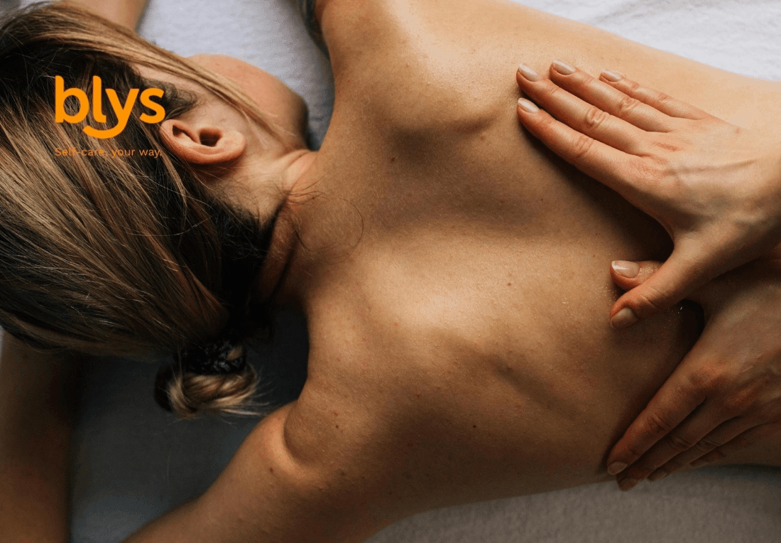 A woman lies face down on a massage table while a therapist’s hands gently massage her bare back lomi lomi style, creating a calm, restorative spa mood.