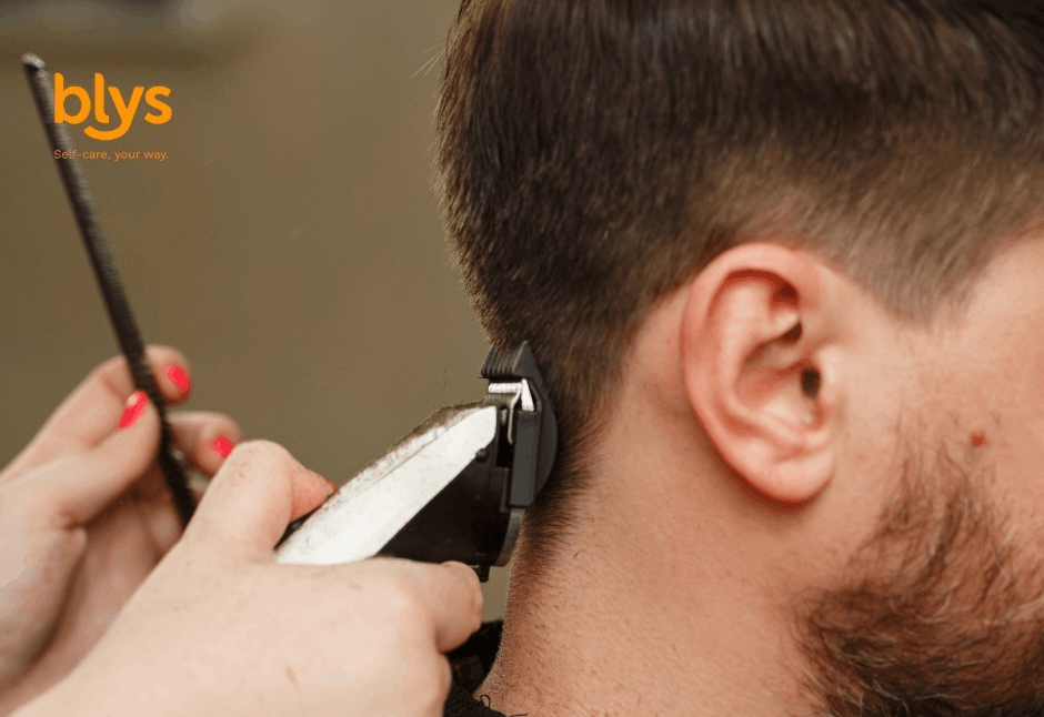 Close-up of a barber using electric clippers and a comb to shape a bearded man's neckline, conveying precision and professional grooming.
