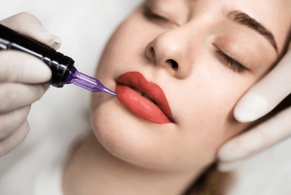 Close-up of a woman receiving cosmetic lip blush tattooing with a purple needle; gloved hands steady her face as red pigment is applied, creating a calm, clinical mood.