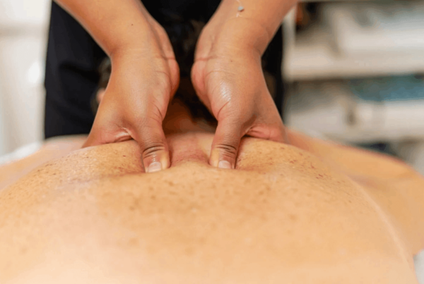 A massage therapist presses both thumbs into a client’s shoulder blades during a trigger point massage, conveying a calm, hands-on wellness and relaxation session for pain between shoulder blades.