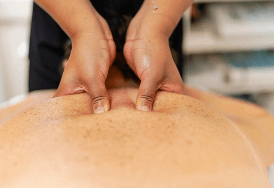 A massage therapist presses both thumbs into a client’s shoulder blades during a trigger point massage, conveying a calm, hands-on wellness and relaxation session for pain between shoulder blades.
