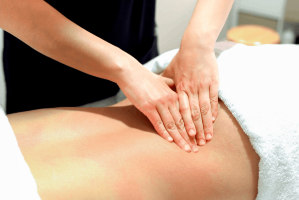 A massage therapist gently presses both hands into a client’s bare lower back for ql pain on a treatment table, conveying calm, soothing relaxation in a room setting.