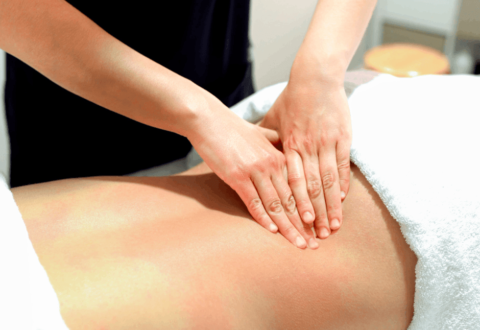 A massage therapist gently presses both hands into a client’s bare lower back for ql pain on a treatment table, conveying calm, soothing relaxation in a room setting.