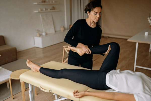A sports massage therapist gently stretches a woman’s bent leg on a massage table in a quiet room, conveying focused, calm rehabilitation care.