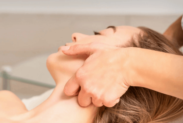 A massage therapist gently massages a woman’s face and jaw as she reclines with eyes closed, creating a calm, soothing TMJ treatment scene.
