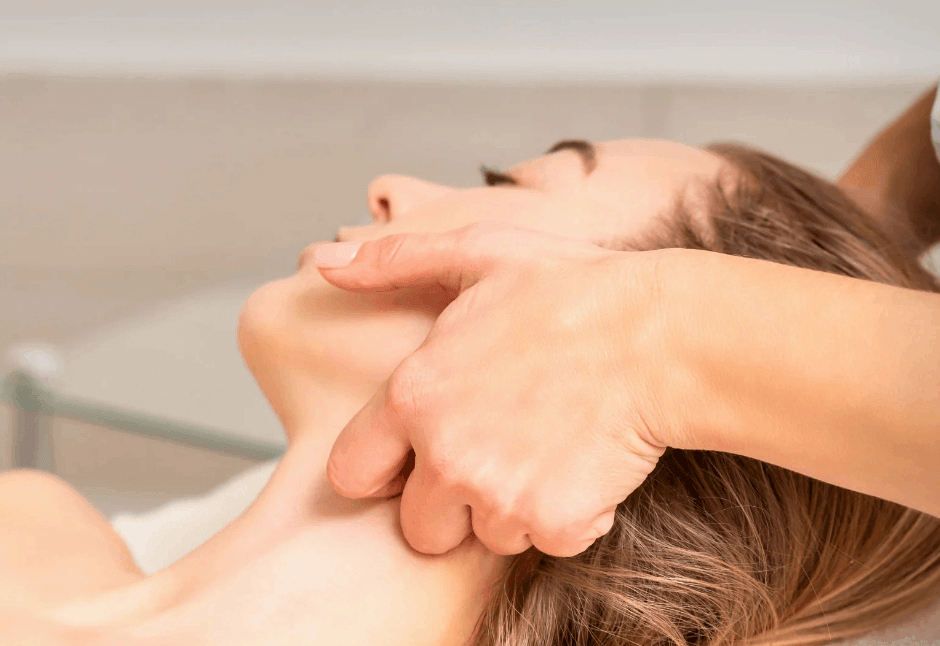 A massage therapist gently massages a woman’s face and jaw as she reclines with eyes closed, creating a calm, soothing TMJ treatment scene.