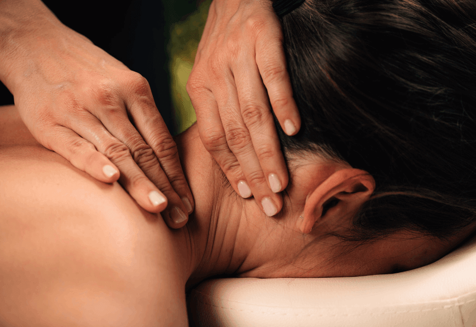 Close-up of hands gently massaging a woman’s neck and shoulder as she lies face down on a massage table, conveying calm and relaxation from forward head posture, rounded shoulders and neck hump from sitting at work.